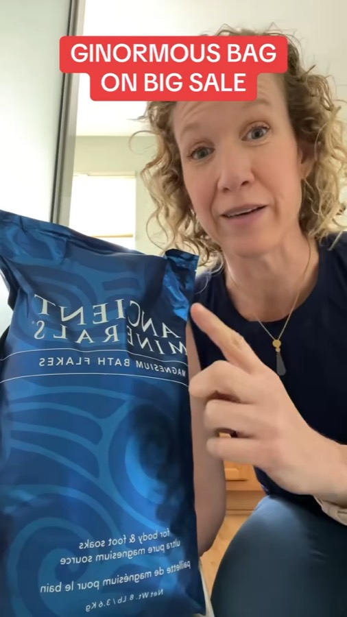 Heather pointing at a large bag of Ancient Minerals magnesium bath flakes under the caption Ginormous bag on big sale